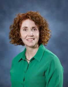 Friendly red-haired woman in green top, holistic health expert, therapeutic services, mind and body wellness.