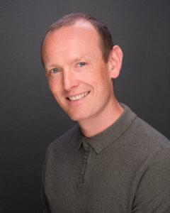 Relaxed man smiling, dark background, health and well-being, therapist portrait, professional mental health care.