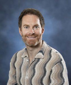 Relaxed man with beard smiling in front of a blue backdrop, wellness and mental health.