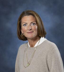 Professional woman with shoulder-length brown hair in a beige sweater and gold jewelry.