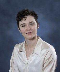Relaxed woman with short curly hair in cream satin shirt, studio portrait.