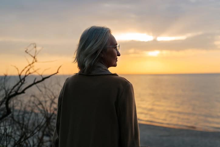 Serene woman watching sunset at the beach, promoting relaxation and mental wellness.