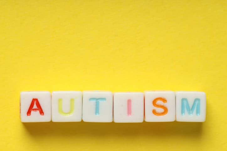 Colourful beads spelling "Autism" on a yellow background, promoting awareness.