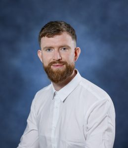 Relaxed man with beard in white shirt against blue background, health and wellness professional.