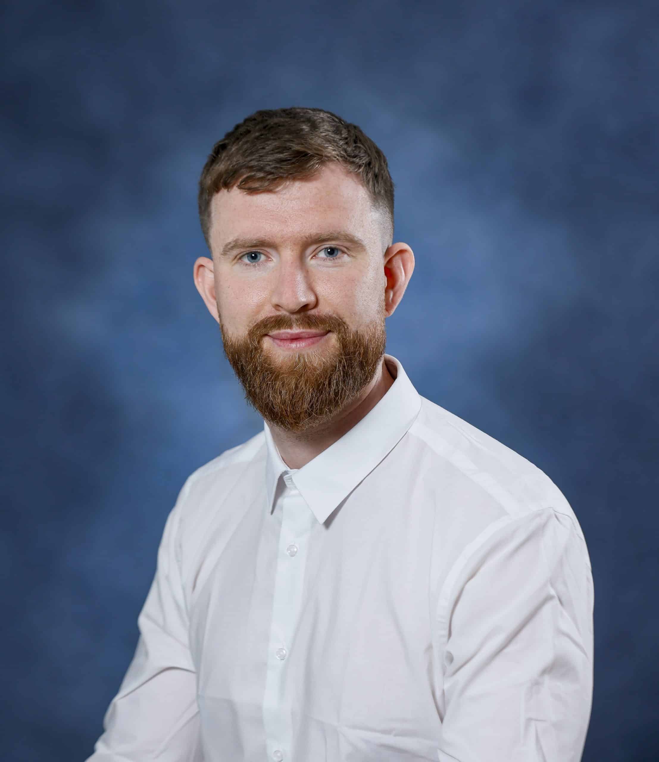 Relaxed man with beard in white shirt against blue background, health and wellness professional.