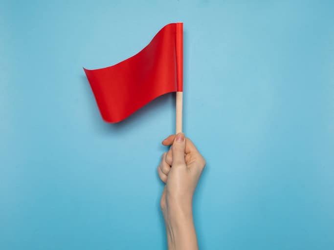 Red flag held by a hand against a blue background, symbolising alert or warning.