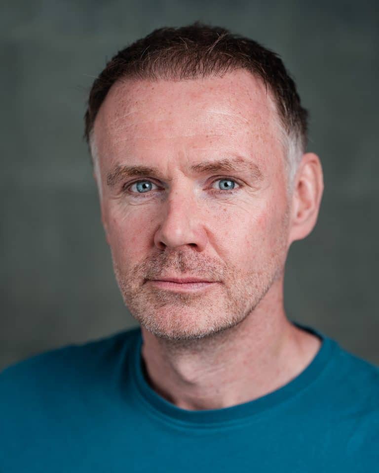 Close-up of a middle-aged man with short brown hair and blue eyes wearing a blue shirt.