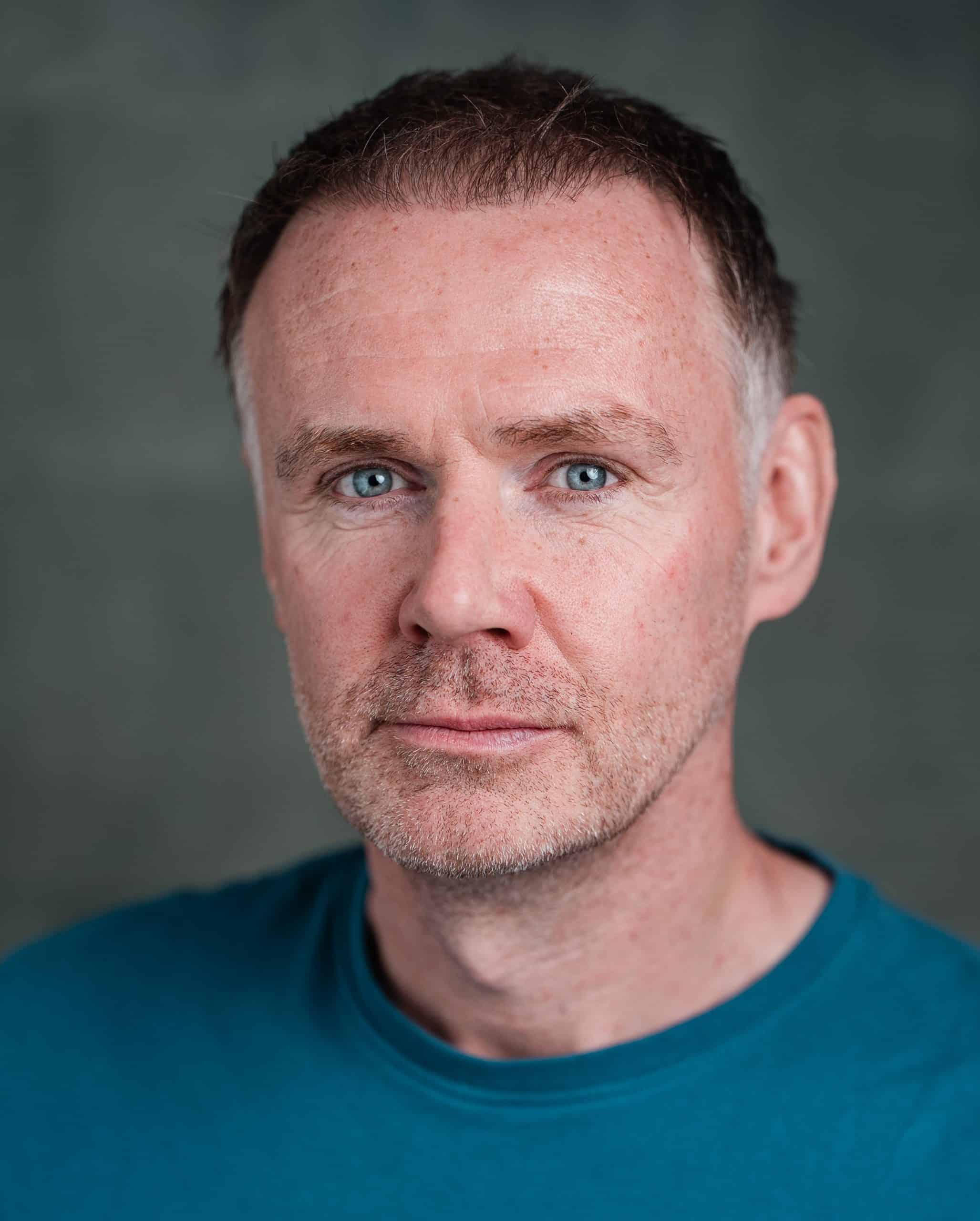 Close-up of a middle-aged man with short brown hair and blue eyes wearing a blue shirt.