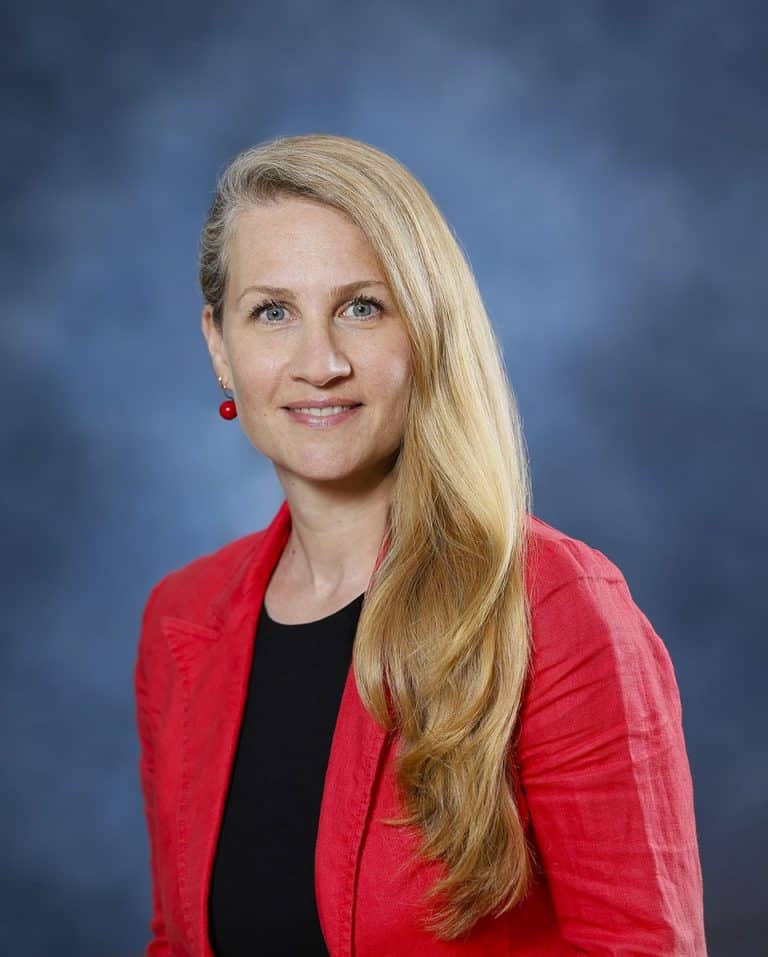 Professional woman with long blonde hair in red blazer smiling at camera.