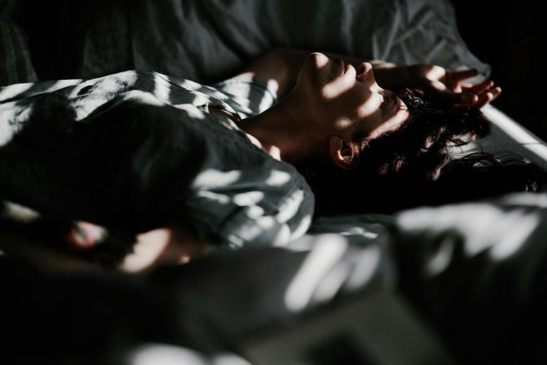 Woman lying in bed with sunlight and shadows, relaxing and resting.