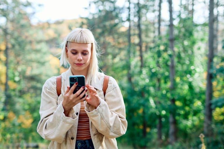 Woman looking at her phone in a lush green forest setting, looking for connections