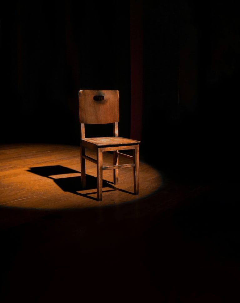 Wooden chair illuminated by a spotlight in a dark room.