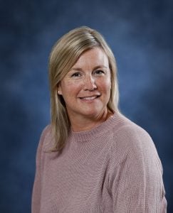 Smiling woman with blonde hair in a pink sweater against a blue background.
