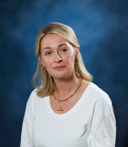 Professional woman with blonde hair in a white top against a blue background.